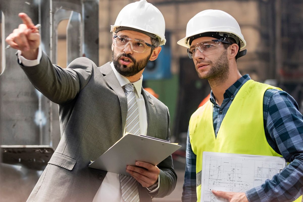 Manager and steel worker talking and looking away in factory